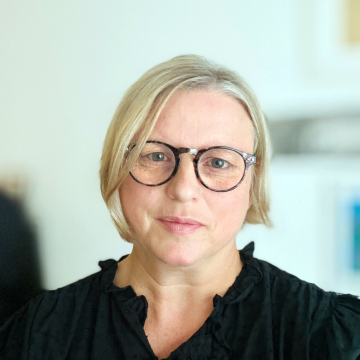 Kreisrundes Foto, das ein Porträt von Barbara Hiltbrunner zeigt. Frau, anfangs 50, helle Haare im Pagenschnitt und Haut, mit Brlle.